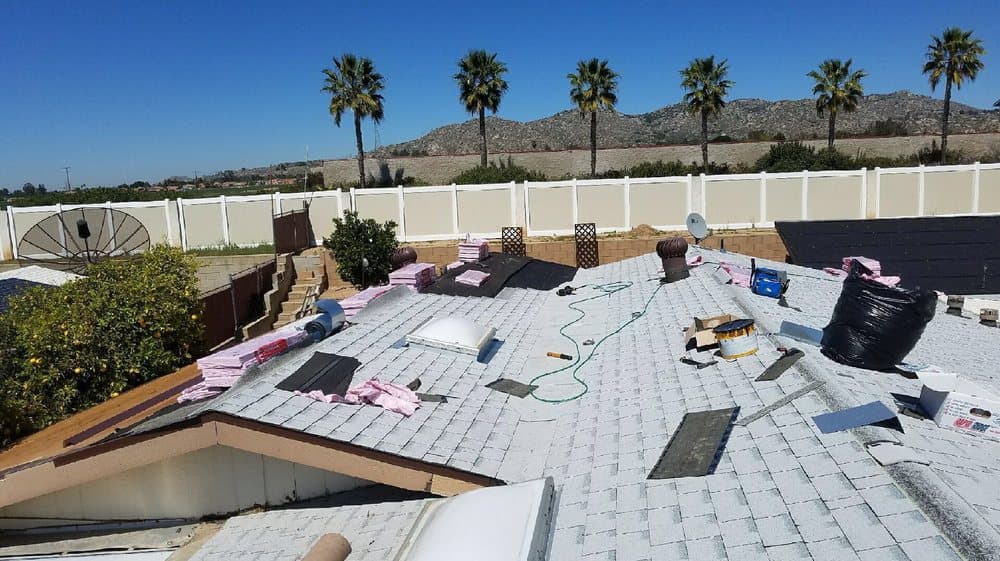 Roof mid tear-off with underlayment rolls staged across the deck